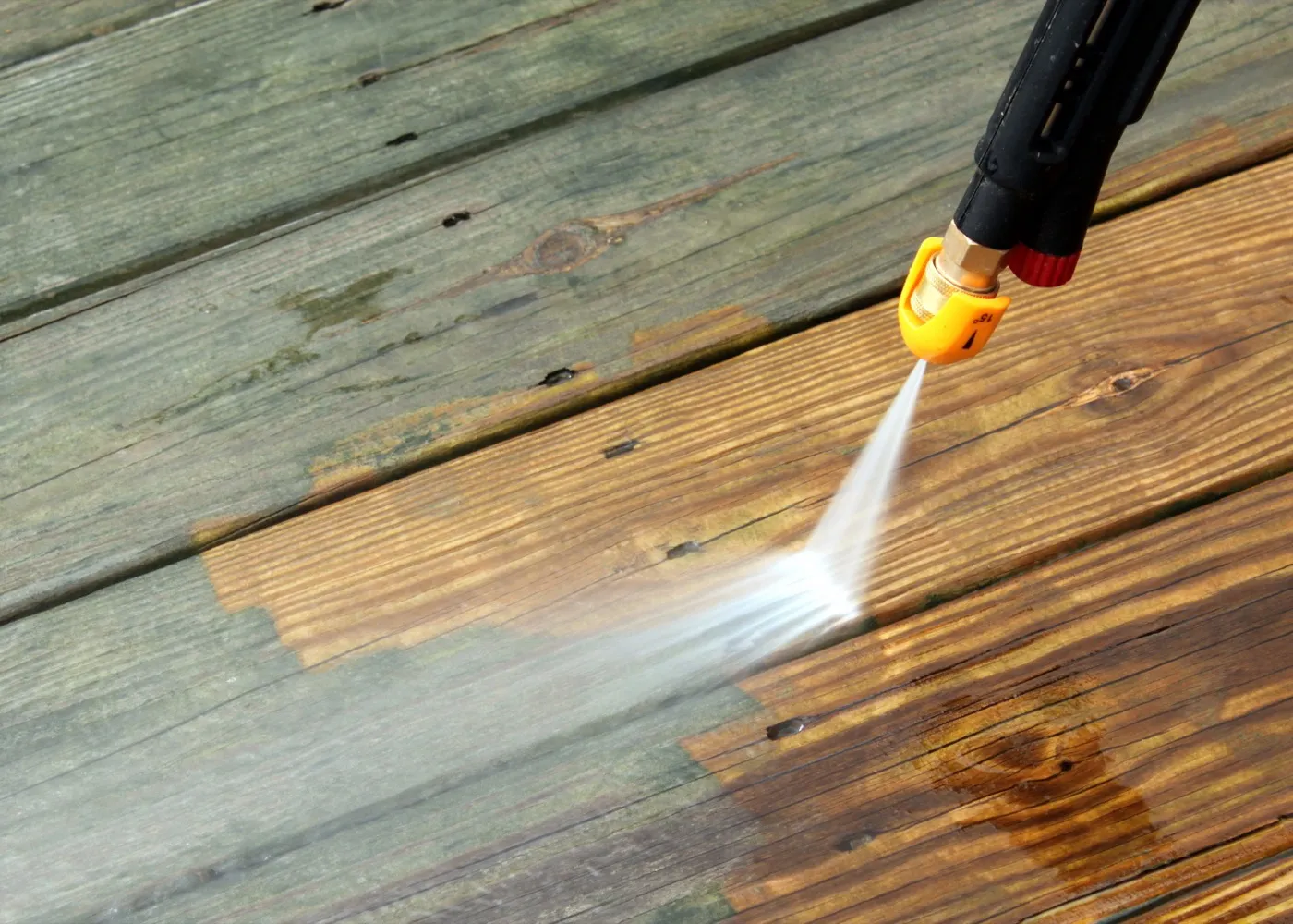 A pressure washer cleaning a weathered wood deck, revealing fresh, clean wood