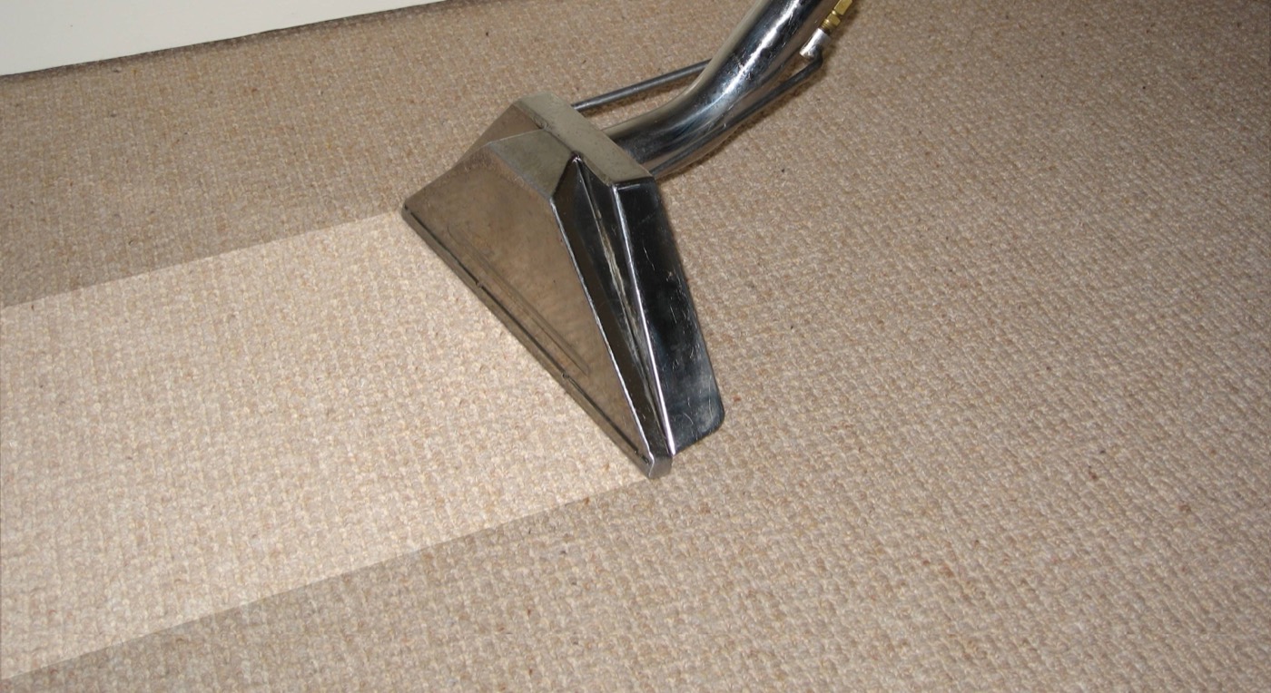 A truck-mounted wand steam-cleaning a carpet, leaving a visibly cleaner strip